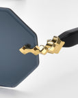 Close-up of Haze sunglasses by For Art's Sake® showcasing black octagonal lenses with gold, jagged metal detail at the frame-temple junction. The faceted edging adds flair, and the black temple provides a striking contrast to the gold accent and ornate temple decorations.