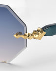 Close-up of For Art's Sake® Haze eyeglass lens with an octagonal shape and silver to blue gradient. It has faceted edging, a decorative gold hinge, and dark green temple arms.