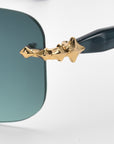 Close-up of For Art's Sake® Edith sunglasses, featuring green-tinted rectangular lenses and a gold star-shaped embellishment on the black frame near the hinge.