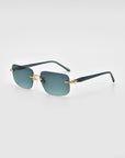 The Edith by For Art's Sake® is a pair of stylish rimless sunglasses with soft rectangular dark green lenses, gold temple accents, and thin black arms, shown against a light gray background.