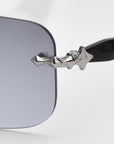 Close-up of For Art's Sake® Edith sunglasses, featuring a black frame and grey rectangular lenses. The arms have a silver star-shaped design near the hinge, part of the Rose Garden collection, emphasizing timeless elegance with unique details.