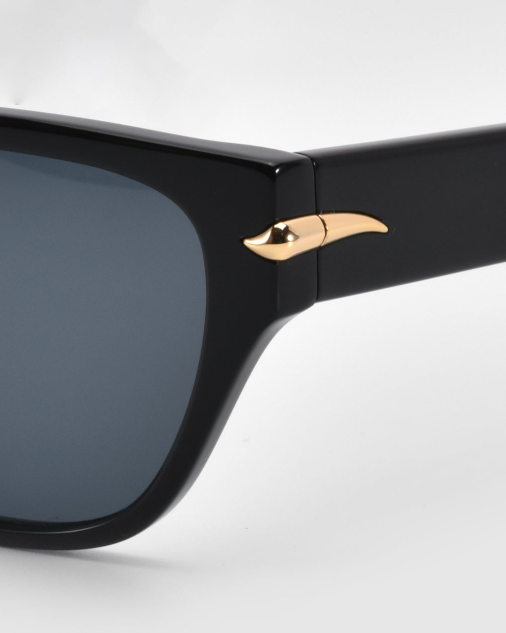 Close-up of the hinge on the Rosie sunglasses from For Art's Sake®, featuring a distinctive gold arrow design. These cat-eye acetate beauties boast black frames and dark lenses, adding elegance to their classic style.