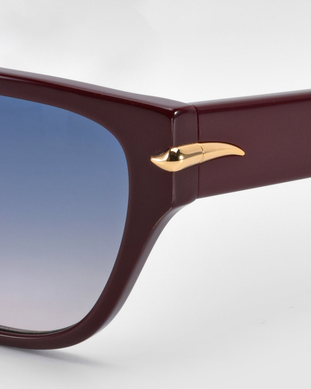Close-up of For Art's Sake® Rosie cat-eye acetate sunglasses with a dark red frame and gold temple accent. The lenses elegantly shift from blue to gray, ideal for everyday wear against a plain white background.