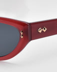 Close-up of For Art's Sake® Lush sunglasses featuring a glossy red frame with geometric facets. The temple arm has two gold pyramid studs near the hinge, and the dark lenses contrast beautifully with the vibrant red, highlighting the premium materials used in their design.