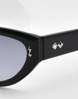 Close-up of the Lush sunglasses by For Art's Sake® features black cat-eye style with a glossy finish, flaunting small silver pyramid studs on the temples near the hinge. Crafted from premium materials, these sunglasses have dark-tinted lenses for a sleek and modern look.