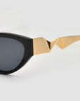 Close-up of For Art's Sake® Unfold sunglasses featuring a unique gold geometric design and pleated temples, set against a plain light gray background.