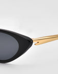 Close-up of the left side of For Art’s Sake® Slash cat-eye sunglasses, featuring a black frame and gold arm, set against a plain light gray background.