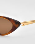Close-up of For Art's Sake® Slash sunglasses: tortoiseshell cat-eye frames with brown lenses and gold metallic arms, inspired by Lucio Fontana, set against a plain light gray background.
