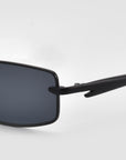 Close-up of For Art's Sake® Lucio sunglasses, highlighting the sleek rectangular design with dark lenses and the left temple against a plain light gray background.