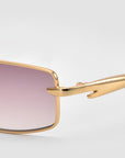 Close-up of For Art's Sake® Lucio sunglasses featuring a sleek gold frame and gradient pink rectangular lenses, set against a light gray background.