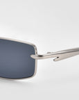 Close-up of For Art's Sake® Lucio sunglasses with a sleek silver metal frame and arms, plus rectangular dark lenses, set against a plain light background.