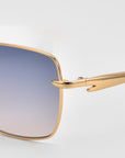 Close-up of For Art's Sake® Edge sunglasses showcasing a sleek square design with a gold frame and gradient blue-to-pink lenses, set against a plain light gray background—perfect for minimalist eyewear lovers.