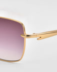 Close-up of For Art's Sake® Edge sunglasses' right side, showing their sleek square silhouette, gold frames, and gradient pink-to-purple lenses. Focus is on the hinge and temple, with a plain gray background highlighting the minimalist design.