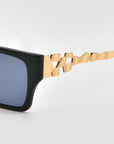 Close-up of For Art's Sake® Incomplete sunglasses with boxy square blue lenses, featuring a unique gold mosaic metal design with geometric jagged shapes, set against a plain light gray background.