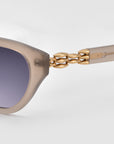 Close-up of The Cuts sunglasses by For Art's Sake®, showcasing a beige weaved metal frame, gradient dark lenses, and gold chain-link detailing on the temples against a plain light background.