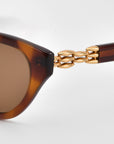 Close-up of The Cuts sunglasses by For Art's Sake®, featuring sculptural tortoiseshell frames and gold chain-link temple detailing, set against a light grey background.