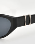 Close-up of Halo(S) sculptural sunglasses by For Art's Sake®, with an acetate frame, dark lenses, and two silver metallic accents near the hinge, shown against a plain light background.