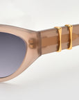 Close-up of For Art's Sake® Halo(S) sculptural sunglasses in taupe acetate with gradient lenses, featuring two gold accents on the arms near the frame.