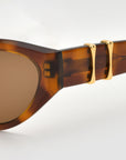 Close-up of For Art's Sake® Halo(S) sunglasses, featuring a sculptural thick acetate frame and gold accents on the temple, set against a light background.