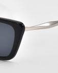 Close-up of the left side of Harmony(S) sunglasses by For Art's Sake®, showing a black rectangular sculptural frame with a sleek silver metal arm, set against a plain white background.