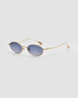 The Calla I by For Art's Sake® are modern oval metal glasses featuring gold frames and blue-tinted lenses, inspired by lightweight sculptural eyewear, shown on a light gray background.