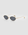 The Calla I by For Art's Sake® are oval-shaped sunglasses with dark lenses and thin gold metal frames. Shown on a light gray background, the image emphasizes their modern, lightweight sculptural design.