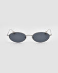 The For Art's Sake® Calla I sunglasses feature a sleek, modern oval metal silhouette with dark lenses and thin silver frames, shown against a plain light gray background.