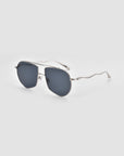 The Lines sunglasses by For Art’s Sake® are oversized aviators with dark lenses, thin silver frames, and wavy sculpted temples, shown angled on a plain light background.