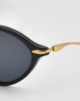 Close-up of For Art's Sake® Totto sunglasses featuring a black acetate and metal frame, sculpted temples, and round dark lenses against a light background.