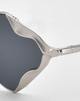 Close-up of For Art's Sake® Leaf I sunglasses featuring dark, diamond-shaped lenses and a sculptural silver wavy frame, showcased against a white background.