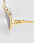 Close-up of For Art's Sake® Tulip II gold-framed sunglasses with black lenses and a sculpted tulip detail at the unique gold hinge, set against a plain light gray background.