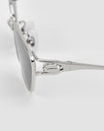 Close-up side view of For Art's Sake® Tulip II: stylish silver sunglasses with reflective lenses and sculpted metal hinge detail on the temple, set against a plain light gray background.