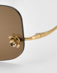 Close-up of For Art's Sake® Magnolia sunglasses featuring brown square lenses, a gold frame, and a decorative gold flower at the hinge.