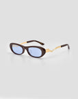 The Abstraction I sunglasses by For Art's Sake® feature oval blue-tinted lenses, thick dark brown chunky frames, and gold accents on the arms, displayed on a plain light gray background.