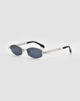 The For Art's Sake® Mesa I sunglasses feature oval dark lenses, silver metal frames, and black temple tips, elegantly displayed on a light grey background to embody quiet luxury.