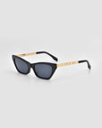 The Mesa II by For Art's Sake® are black luxury cat-eye sunglasses with gold temple accents and dark lenses, crafted from premium acetate and showcased against a plain light gray background.
