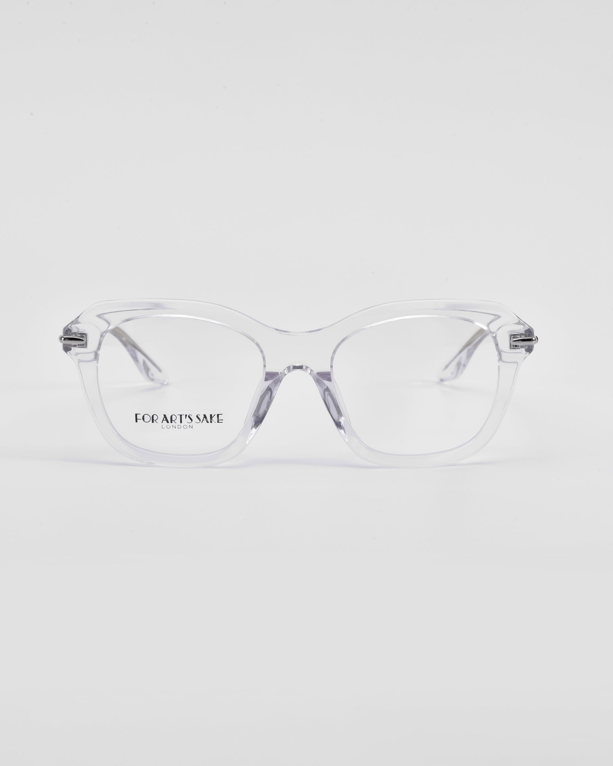 A pair of clear eyeglasses with transparent frames and a hint of a cat-eye silhouette rest on a white surface. The lenses have the text "For Art's Sake® Helene" printed on the left side. The design is minimalist and modern, with slightly thick frames and a subtle, elegant appearance.