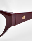 Close-up of Rosalia I glasses by For Art's Sake® from the Rose Garden Collection featuring a deep red cat-eye frame with gold, rose-shaped embellishments on the temple. These glasses exude femininity and offer a sleek, modern design against a white background.