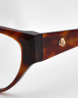 Close-up of the side of a bold, brown tortoiseshell cat-eye optical frame from the Rosalia I by For Art's Sake®. The arm features a small, gold rose emblem against a plain, light grey background.