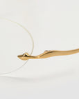 A close-up of the For Art's Sake® Waver gold minimalist eyeglass frame with rimless lenses, showcasing the elegant curved temple and seamless arm-to-lens connection against a white background.