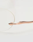 Close-up of For Art's Sake® Waver eyewear with a rose gold curved metal temple and clear lens, highlighting the minimalist, lightweight frames against a clean white background.