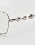 Close-up of For Art's Sake® Fluid: a silver eyeglass frame with a 3D fluid design on the temple arm and soft-square lenses, shown against a plain white background.