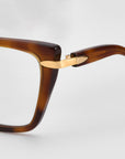 Close-up of the top corner and arm hinge of For Art's Sake® Motion I brown rectangular frames, featuring gold-tone metal accents at the hinge and acetate temples against a plain light background.