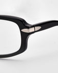 Close-up of the hinge and arm of the For Art's Sake® Motion II black eyeglass frames, featuring a small silver metal accent on the hinge and curved acetate temples, set against a plain white background.
