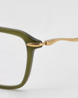 Close-up of the Claudia eyeglass frame by For Art's Sake® with an olive green rectangular acetate and metal front and sleek gold sculpted temples, set against a plain light background.