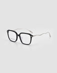 The Claudia eyeglasses by For Art’s Sake® feature black rims, clear lenses, and distinctive wavy silver sculpted temples in acetate and metal, shown on a light gray background.