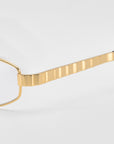 Close-up of the gold, textured arm of the Iris geometric rectangular eyewear by For Art's Sake®, set against a plain light gray background.