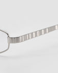 Close-up of For Art's Sake® Iris frames featuring sculptural metal with a textured, grooved temple arm, set against a plain light gray background.