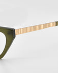 Close-up of For Art's Sake® Lavender cat-eye acetate glasses, featuring a dark green frame and metallic textured gold temple arm, embodying quiet luxury against a plain light background.