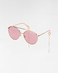 For Art's Sake® Yoyo - ARC sunglasses are gold-framed aviators with rose-tinted lenses and pink earpieces, adorned with chains featuring pearl accents. The 18-karat gold-plated design exudes luxury against a plain white background.